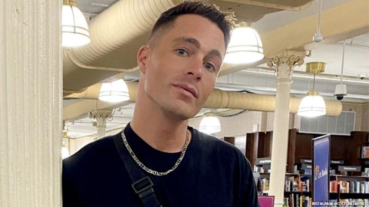 Colton Haynes poses in a black t shirt and chain necklace.