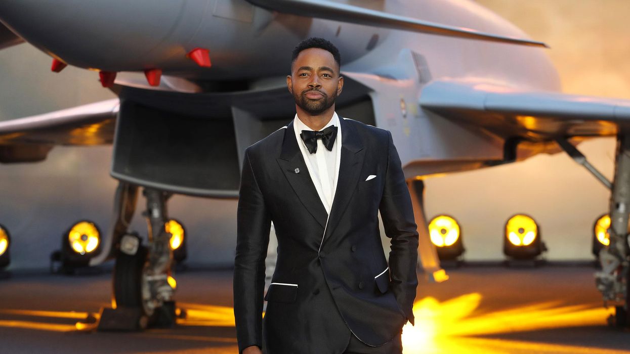 Jay Ellis poses in a suit in front of a plane 