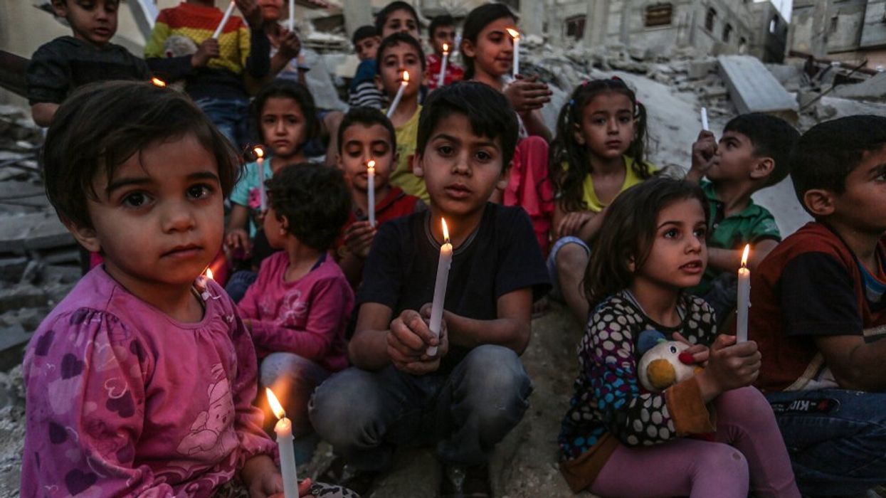 Palestinian children hold candles in the rubble of a house destroyed in Israeli airstrikes